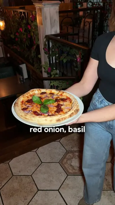 A stone-baked nduja pizza with red onion and basil, carried to the table